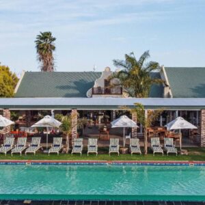 A resort with a pool and chairs and a building at Mooiplaas Guesthouse in Oudtshoorn