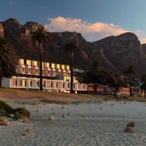 A building on a beach with palm trees and mountains at Morea House, Autograph Collection in Cape Town