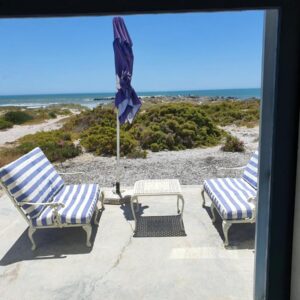 Two loungers and a table on a patio facing the beach at Nieuview Cottages in Paternoster