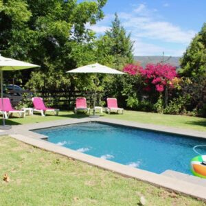 A swimming pool with chairs and umbrellas in a yard at Nuwerus Lodge Paarl in Paarl