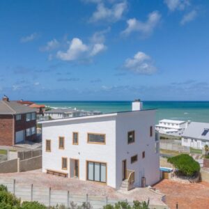A white house with the ocean in the background at Oom Jan Guesthouse in Struisbaai