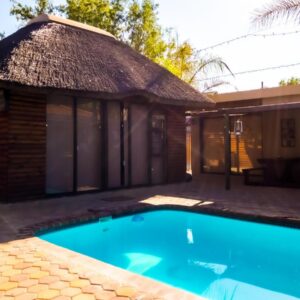 A house with a swimming pool in front of a building at Oppi Draai Guesthouse in Oudtshoorn