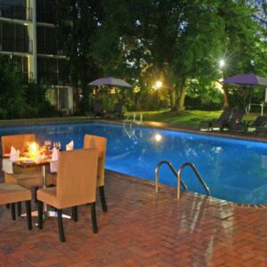 A table and chairs next to a swimming pool at night at Oudtshoorn Inn Hotel in Oudtshoorn