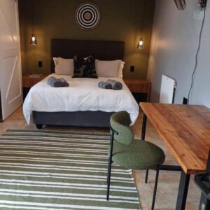 A bedroom with a bed and a wooden table and a table and chair at Oystercatcher Guest House in Wilderness