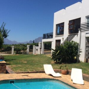A house with a swimming pool and two white chairs at Paarl Mountain Lodge in Paarl