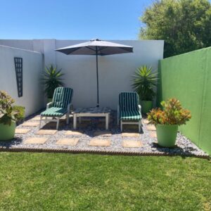 A patio with two chairs and a table and an umbrella at Palm and Pebbles self catering cottages Paternoster in Paternoster