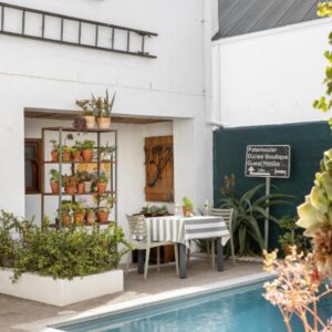 A pool in front of a white building with a table at Paternoster Dunes Boutique Guesthouse in Paternoster