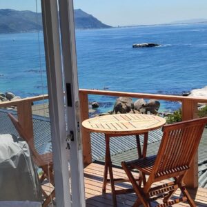 A table and chairs on a balcony with the ocean at Penguins View Guesthouse in Simonʼs Town