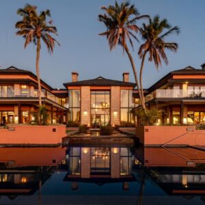 A large house with palm trees in front of a body of water at Pezula Nature Retreat in Knysna