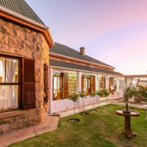 A stone house with a courtyard with a table and chairs at Ravenscliff Manor in Oudtshoorn