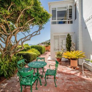 A patio with green chairs and a table and a tree at Salop House in Fish hoek