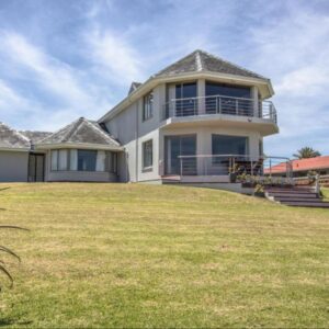 A large house on top of a grassy hill at Sandbaai Country House in Hermanus