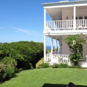 A white house with a balcony and a lawn at Southern Cross Beach House in Plettenberg Bay