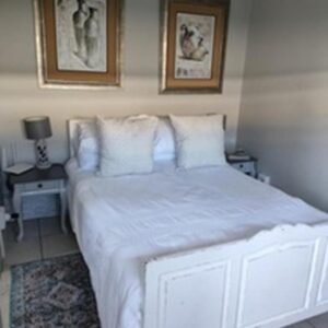 A bedroom with a white bed with two pictures on the wall at Stonehenge Cottage in Oudtshoorn