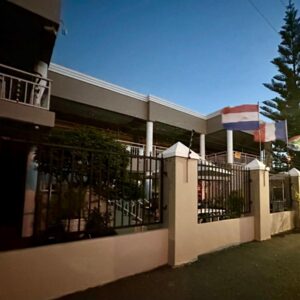 A building with a fence and a tree and a flag at Sunset Boulevard Riverlodge in Paarl