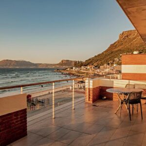 A balcony with a table and chairs and the ocean at Surferscorner Self Catering Apartments in Muizenberg