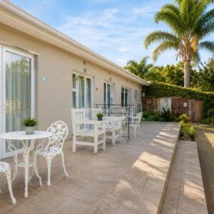 A patio with white tables and chairs and a palm tree at The Alchemist's Place in Oudtshoorn