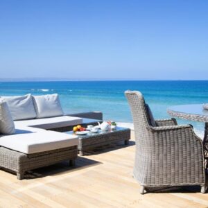 A patio with wicker chairs and a table and the ocean at Bay Lodge on the Beach in Mossel Bay
