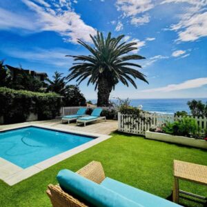 A backyard with a pool and a palm tree and the ocean at The Clarendon - Bantry Bay in Cape Town