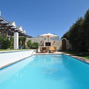 A swimming pool with an umbrella and a chair at The Gables Hermanus in Hermanus