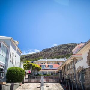 White and stone buildings along a lane with a mountain behind at The Majestic Apartments in Kalk Bay