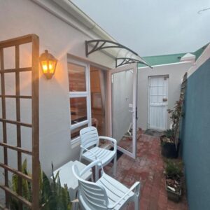 A patio with two white chairs and a lamp at The Muizenberg Muse in Muizenberg