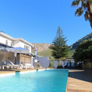 A swimming pool next to a house with a palm tree at THE PLACE Muizenberg in Muizenberg