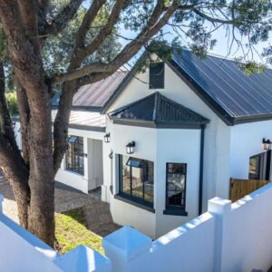 A white house with a fence and a tree at The Wellington Residence in George