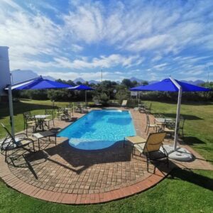 A pool with chairs and tables and blue umbrellas at Town Lodge George in George