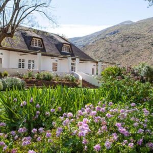 A large white house with flowers in front of it at Varkenskraal Farm in De Rust
