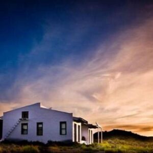A white house in a field with a sunset at Vrisch Gewagt Boutique Self-Catering Olive Farm in Prince Albert