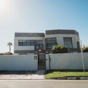 A house with a white fence and a gate at Wave Inn Guesthouse in Valsbaai