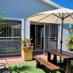 A wooden table and an umbrella on a patio at Winderuis Kite and Wing Cottage in Langebaan