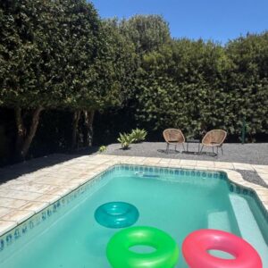 Three frisbees in a swimming pool with three chairs at Wood Road Coastal Guest rooms in Hout Bay