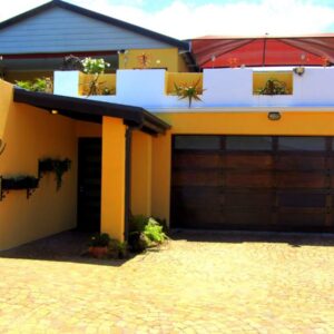 a Vue Guesthouse: a yellow house with a garage and a red umbrella