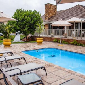 Avanti Guest Lodge: a swimming pool with chairs and umbrellas next to a house