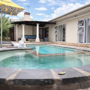 Cammy's Guesthouse: a swimming pool with an umbrella in front of a house