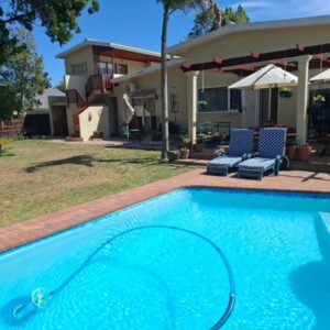 Cedar Lodge Guest House: a swimming pool with two chairs and a house