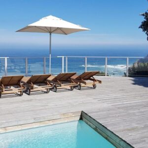 Headlands House Guest Lodge: a deck with chairs and an umbrella and the ocean