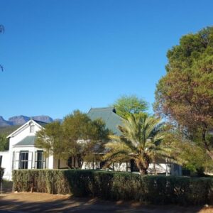 Klaarstroom Guest House: a white house with trees and mountains in the background