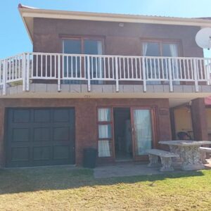 Mossel Bay Self Catering Family Units: a house with a balcony and a table in front of it
