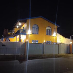 Neo & Ruks Sleep & Go Parow: a yellow house with a fence in front of it at night