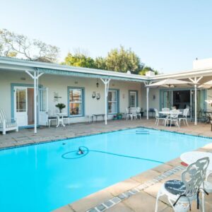 Paradiso Guesthouse & Self-catering Cottage: a swimming pool with chairs and tables in front of a house