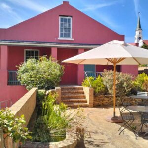 The Restio Country Guesthouse: a red house with a table and an umbrella