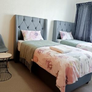Twinex Accommodation Bellville: a bedroom with two beds and a chair and a window