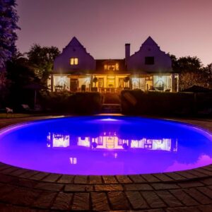 Vredenburg Manor House: a large blue swimming pool in front of a house